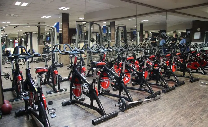 سالن بدنسازی و اسپینینگ مجموعه ورزشی و استخر برادران محبی: ردیف‌های منظم دوچرخه‌های ثابت مشکی و قرمز برای تمرین هوازی.