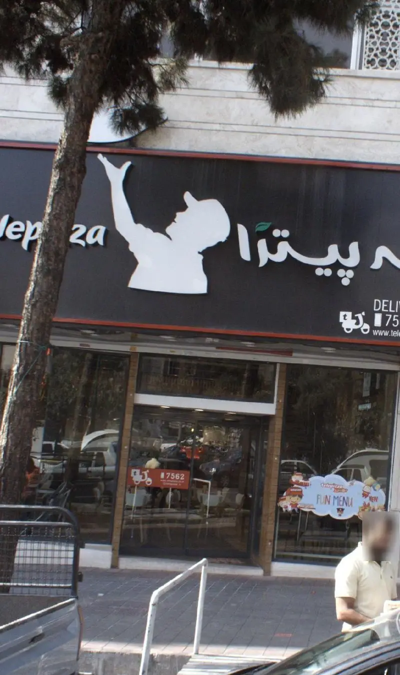 نمای بیرونی و سردر شعبهی تله پیتزا در تهرانپارس با لوگوی مرد و متن تله پیتزا، همراه با اطلاعات دلیوری و منوی جدید پیتزا.