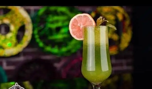 نوشیدنی سبز خوشرنگ و خنک، اسموتی میوه تازه با برش گریپ فروت و برگ نعناع در لیوان بلند. ارائه شده در فضای مدرن و دلپذیر کافی شاپ پارکینگ.