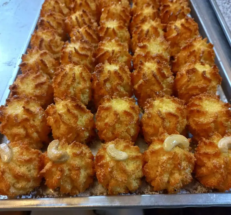 شیرینی نارگیلی طلایی و خوشرنگ قنادی تیک وتیک، با بافت شیاردار و مغز بادام هندی، مناسب برای پذیرایی.