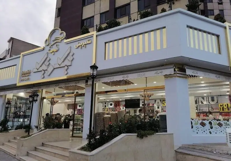 نمای بیرونی قنادی مدرن تیک و تیک، شیرینی فروشی لوکس با دکوراسیون طلایی و ورودی پله‌ای، عرضه کننده انواع شیرینی، کیک، آجیل و خشکبار.