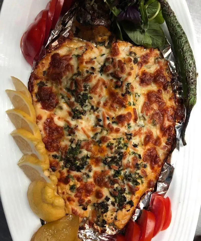 یک پرس ماهی پخته شده پنیری خوشمزه با روکش طلایی پنیر، سبزیجات معطر و لیمو در رستوران ایرانی نمونه تهران.