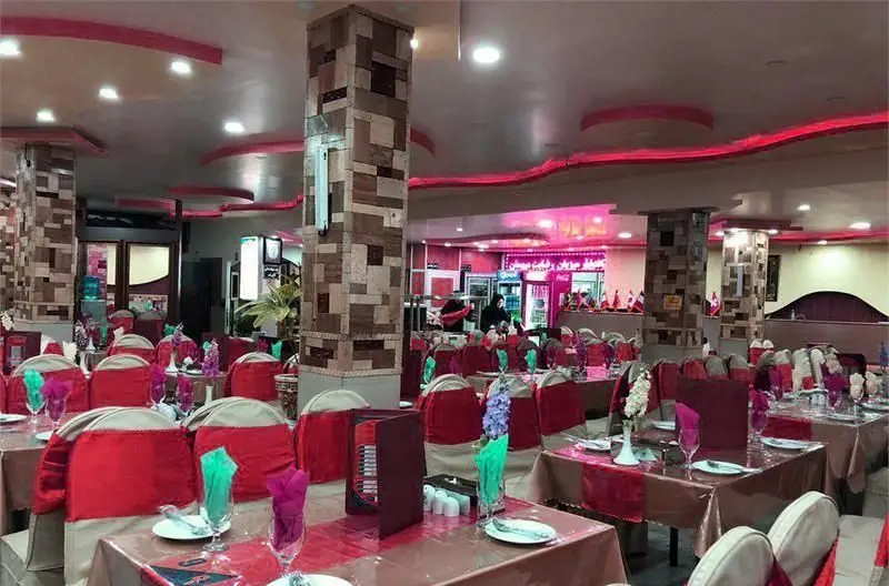 دکوراسیون داخلی رستوران ایرانی نمونه تهران با ست میز و صندلی‌های چیدمان شده، نورپردازی مدرن و ستون‌های سنگی زیبا برای پذیرایی.