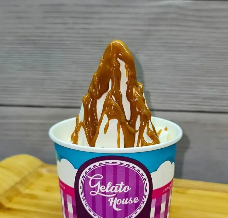 یک لیوان جلاتو خامه‌ای سفید خوش‌طعم و تازه با روکش سس کارامل طلایی و جذاب، از محصولات ویژه خانه جلاتو و دسر عالی.