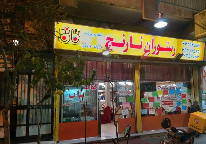 نمای بیرونی رستوران نارنج با تابلو زرد روشن و نام فارسی، شماره تلفن‌ها، و لوگوی نارنج. موتور سیکلت بیرون‌بر در جلو. ارائه انواع غذای ایرانی و کباب.