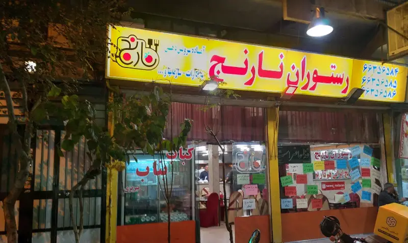 نمای شبانه رستوران نارنج با تابلوی روشن، شماره تماس و لوگوی غذاخوری. ارائه دهنده غذای ایرانی و کباب برای سفارش حضوری و بیرون بر.
