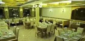 نمایی زیبا از سالن غذاخوری رستوران قصر موج با میزهای چوبی شیک، صندلی‌های راحتی، چیدمان کامل، نورپردازی گرم و فضایی دلباز.