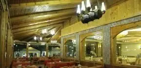 فضای داخلی دلباز رستوران قصر موج با سقف چوبی، لوسترهای چشمگیر، میزهای چیدمان شده و محیطی آرام برای تجربه غذایی دلپذیر.