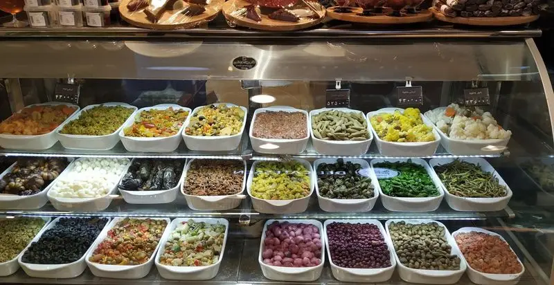 ویترین جذاب دی مارت پر از انواع غذاهای سلف سرویس شامل سالادهای تازه، ترشیجات، زیتون و غذاهای خوشمزه آماده.