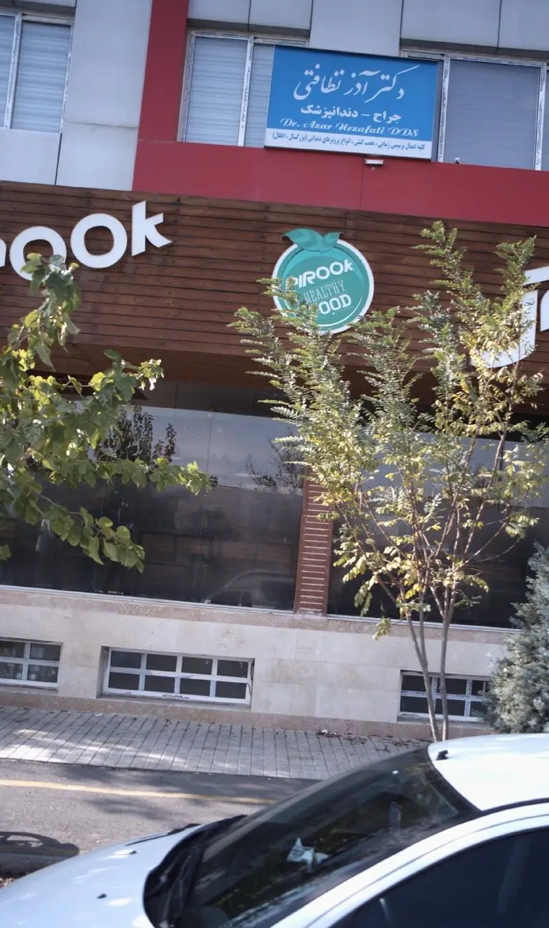 نمای سردر و ورودی رستوران پیروک هلثی فود با تابلوی سبز و لوگوی شرکت، ارائه دهنده غذای سالم و پیتزا. منظره خیابان.