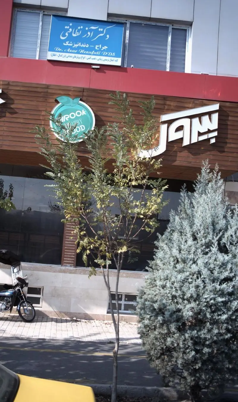 نمای خارجی رستوران پیتزا پیروک (PIROOK HEALTHY FOOD) با لوگوی سیب سبز. بالای آن، مطب دکتر آذر نظافتی، جراح دندانپزشک، دیده می‌شود.