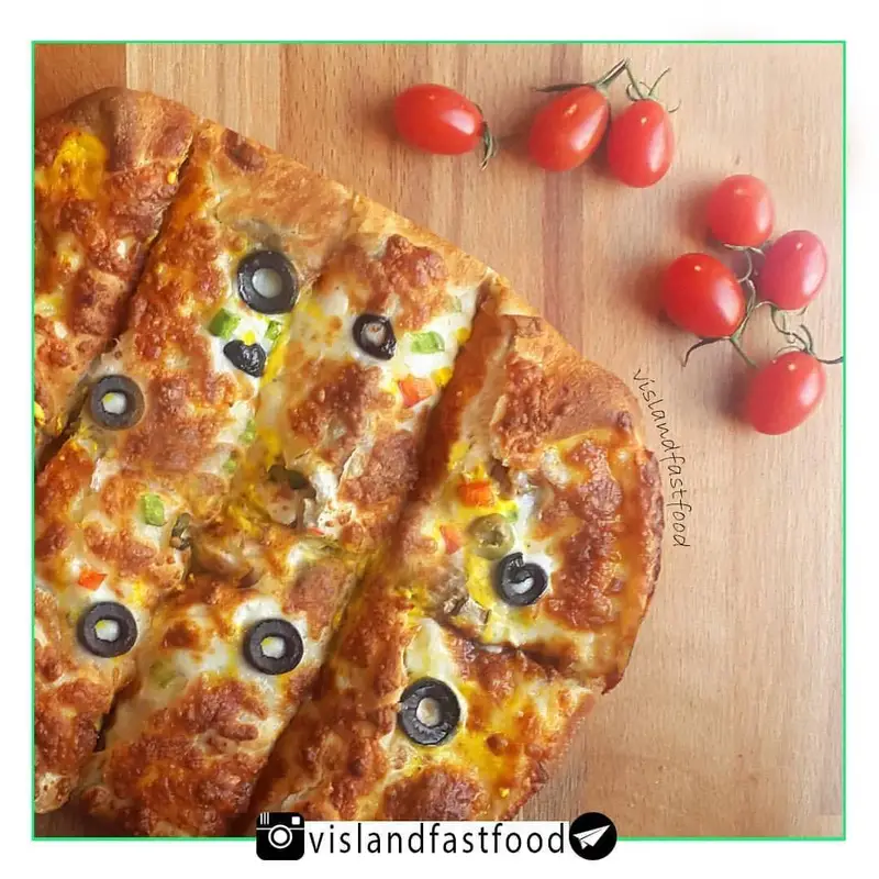 پیتزای لذیذ و پرپنیر ویسلند با زیتون و فلفل دلمه‌ای رنگی، آماده سرو روی تخته چوبی در کنار گوجه فرنگی‌های تازه.