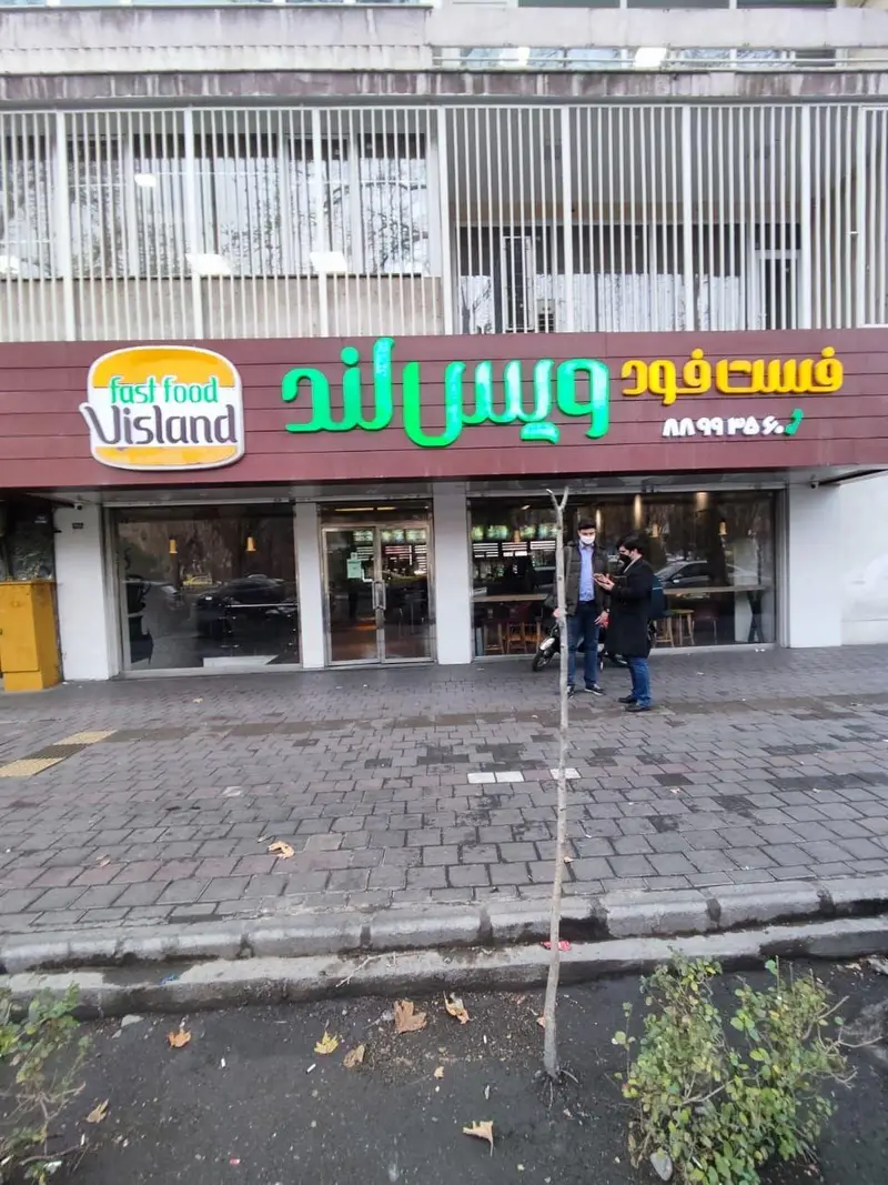 تصویری از نمای بیرونی فست فود ویسلند، با تابلوی روشن نام و لوگو، و شماره تلفن ۸۸۹۹۳۵۶۰ برای سفارش آنلاین غذا.