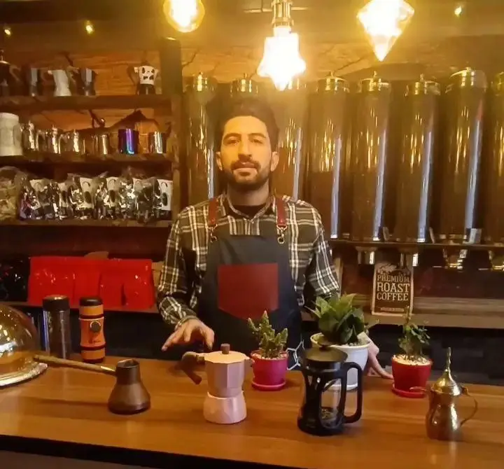 باریستای حرفه‌ای کافه جوان، با نمایش موکاپات، فرنچ پرس و جذوه، آماده برای ارائه بهترین قهوه‌های تازه و دانه‌های رست شده.