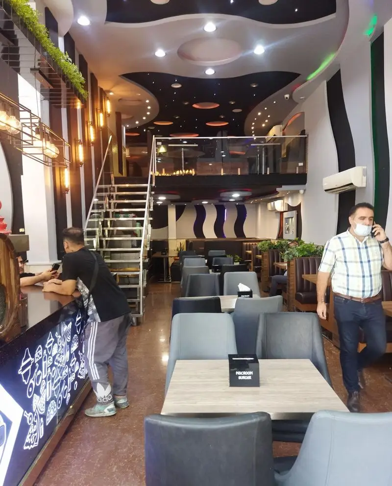 فضای داخلی لوکس و مدرن رستوران پیتزا مکروم با طراحی دو طبقه، سقف خاص و نورپردازی زیبا، همراه با میز و صندلی‌های راحت.