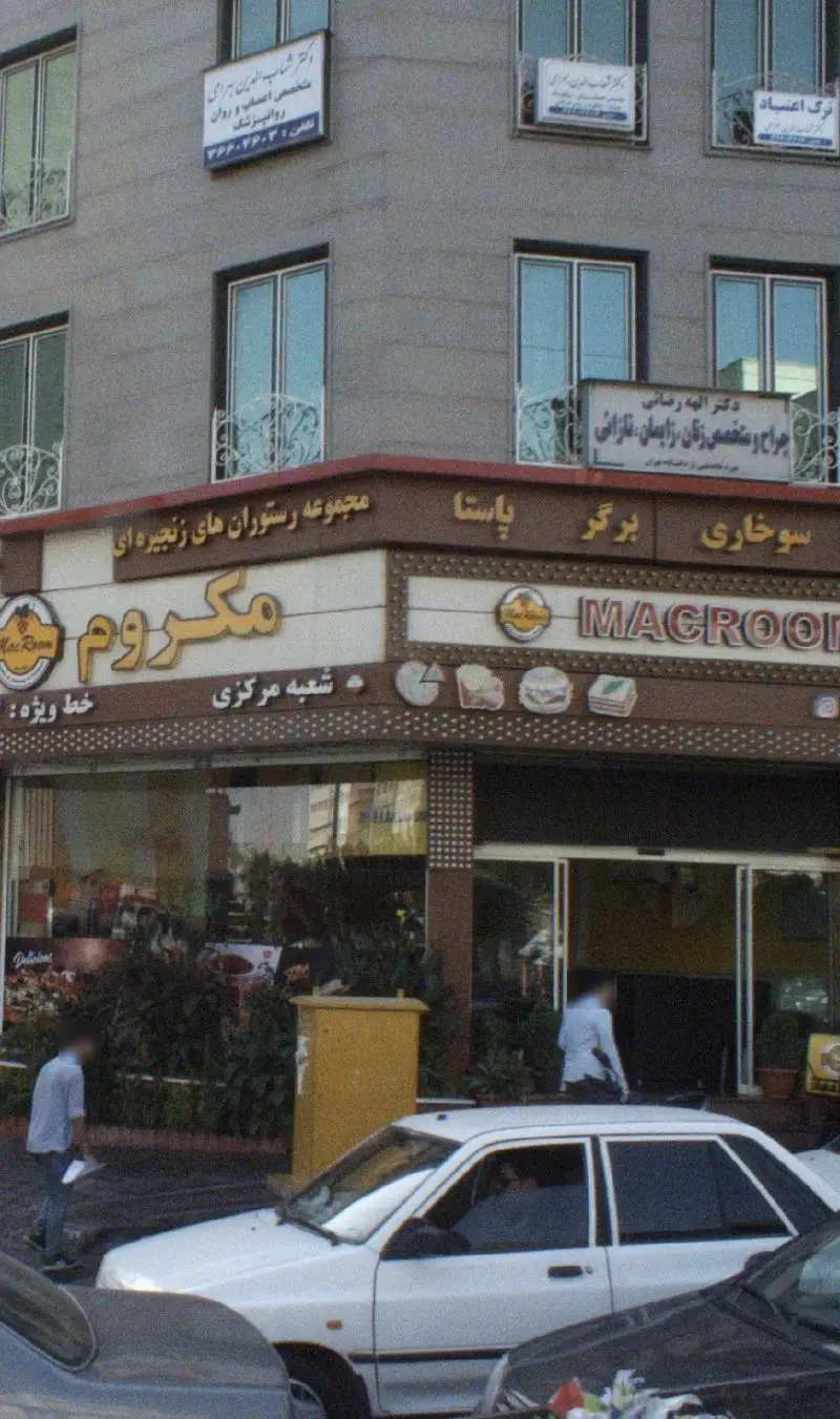 تصویری از نمای بیرونی رستوران مک روم، ارائه دهنده انواع پیتزا، پاستا، برگر و سوخاری، در یک خیابان شلوغ با ماشین‌ها.