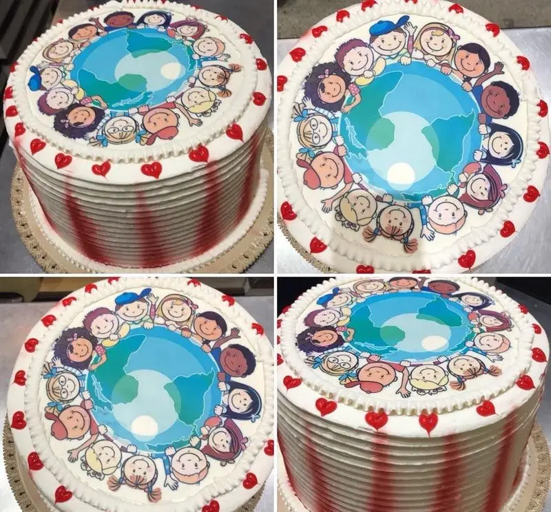 کیک سفید کافه قنادی لادن با طرح خوراکی کودکان متنوع دور کره زمین، نماد صلح و دوستی، تزئین شده با نوارهای قرمز و قلب‌های لبه.