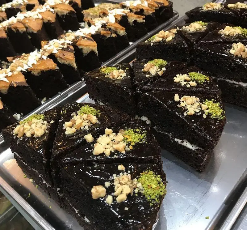 نمایش جذاب انواع کیک شکلاتی و شیرینی‌های لذیذ کافه قنادی لادن، تزئین شده با پسته و گردو. دسرهای تازه و باکیفیت برای مشتریان.