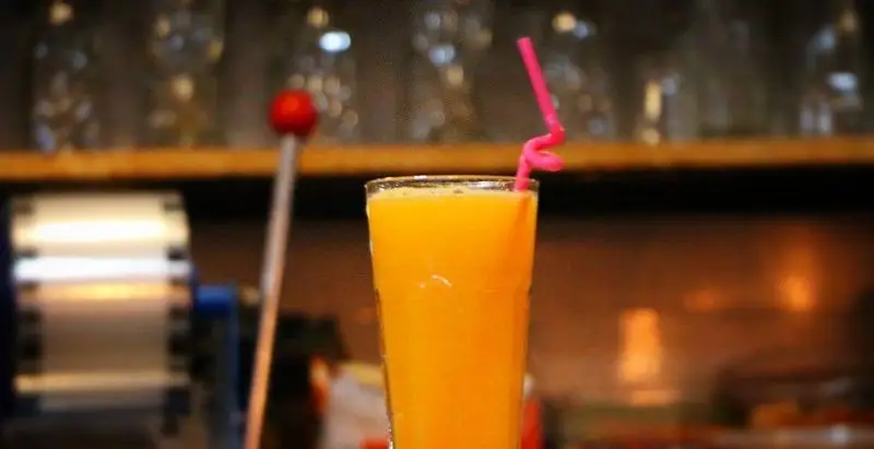 لیوانی پر از آب پرتقال طبیعی و تازه با نی صورتی رنگ در محیط گرم و دلنشین کافه بستنی بابا علی، نوشیدنی خنک و سرشار از ویتامین سی.