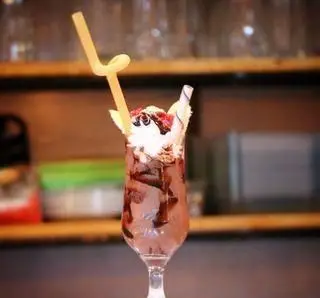 دسری لذیذ از بستنی بابا علی: بستنی یا میلک شیک شکلاتی در لیوان پایه بلند با خامه فرم گرفته، موز و سس شکلات.