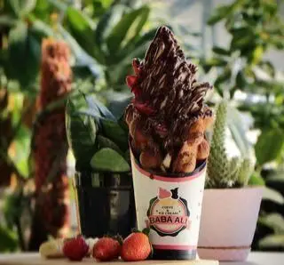 بستنی قیفی شکلاتی غلیظ و مخصوص کافه بستنی بابا علی با تزئینات توت فرنگی و دسر خوشمزه در محیطی سبز و دلنشین.