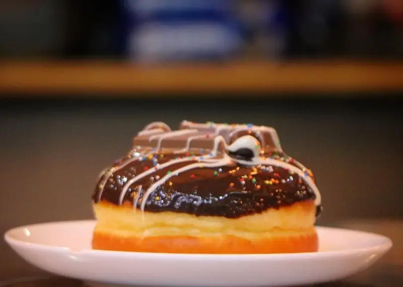 دونات شکلاتی ویژه و لذیذ با تزئینات رنگی و شکلات کیت کت، محصولی دلپذیر از منوی متنوع بستنی بابا علی.