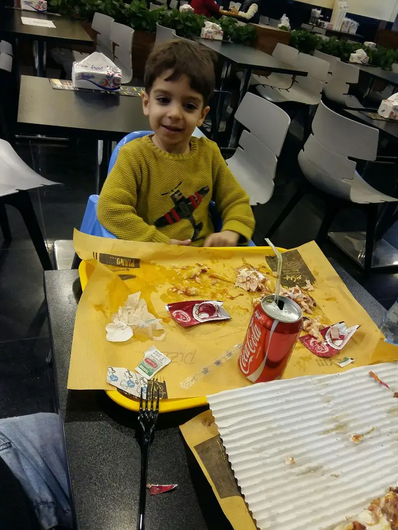 کودک خندان در حال غذا خوردن در رستوران پیانو. پس از یک وعده پیتزا و غذای دیگر، میز پر از باقی مانده غذا است. لذت بردن در محیط خانوادگی.