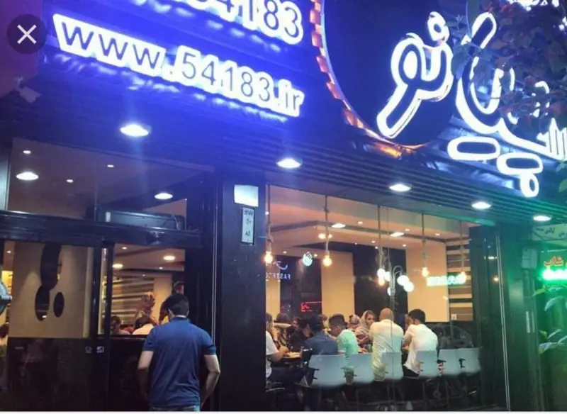 تصویر نمای بیرونی رستوران پیانو با تابلوی نئون جذاب و درخشان. مشتریان در حال غذا خوردن داخل دیده می‌شوند. آدرس: www.54183.ir