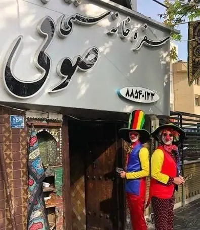 نمای بیرونی سفره خانه سنتی صوفی در تهران با تابلوی نام و شماره تلفن ٨٨٥٣٠١٣٣ و دو دلقک با لباس‌های رنگی در ورودی آن