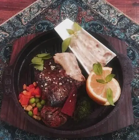 تجربه طعم بی‌نظیر استیک یا کباب گریل شده در ماهیتابه چدنی، با سس ویژه، سبزیجات تازه و پرتقال در سفره خانه سنتی صوفی.