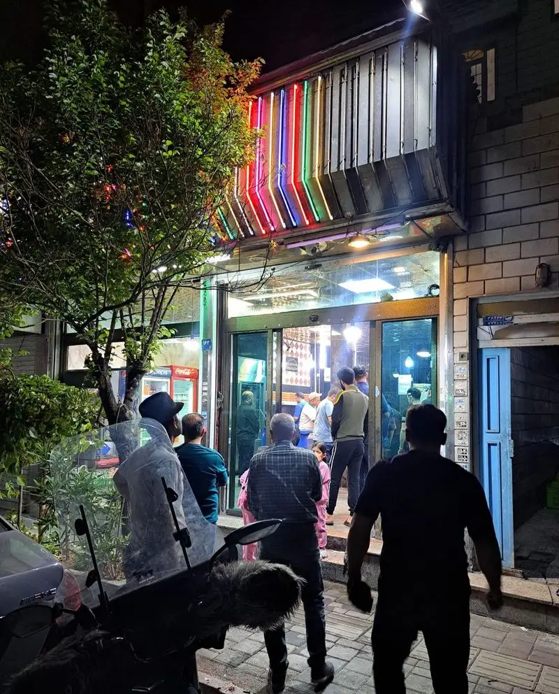 تصویر کسب و کار کبابی ابوالفضل در شب با نورپردازی نئون جذاب، میزبان مشتریان فراوان برای کباب‌های اصیل و غذای ایرانی.