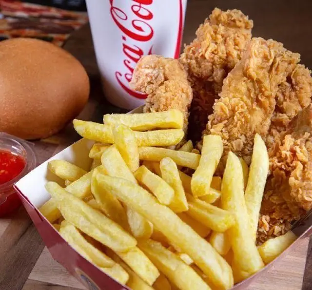 یک وعده غذای کامل از مرغ سوخاری چیکن ترد و طلایی به همراه سیب‌زمینی سرخ کرده، نوشابه و نان برای تجربه‌ای خوشمزه.