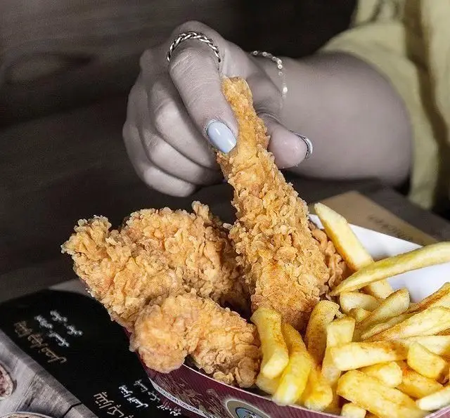 تصویر جذاب از دست در حال برداشتن مرغ سوخاری ترد و کریسپی چیکن همراه با سیب زمینی‌های طلایی، تجربه فست فود بی‌نظیر.