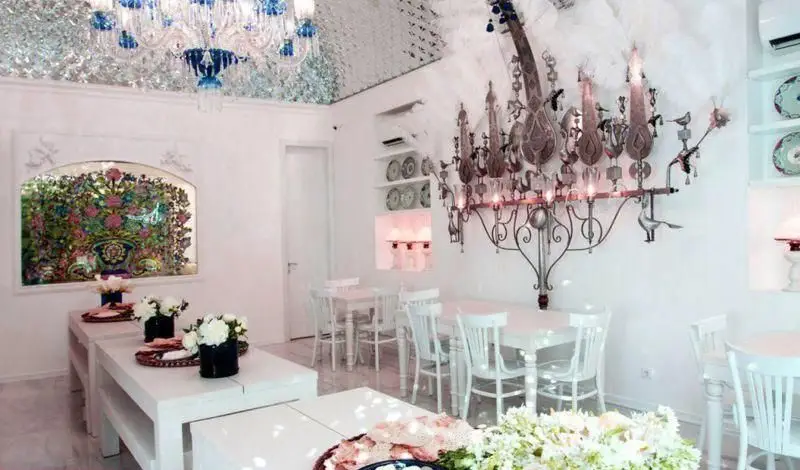 فضای داخلی روشن و منحصر به فرد رستوران دلی جان با لوسترهای کریستالی و فلزی خاص، سقف براق و میزهای سفید.