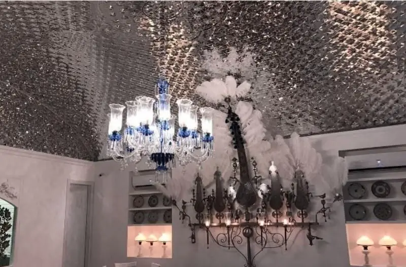 دکوراسیون داخلی مجلل و چشمگیر رستوران دلی جان با سقف شیشه‌ای خیره‌کننده، لوستر کریستالی و دیوارکوب‌های هنری.