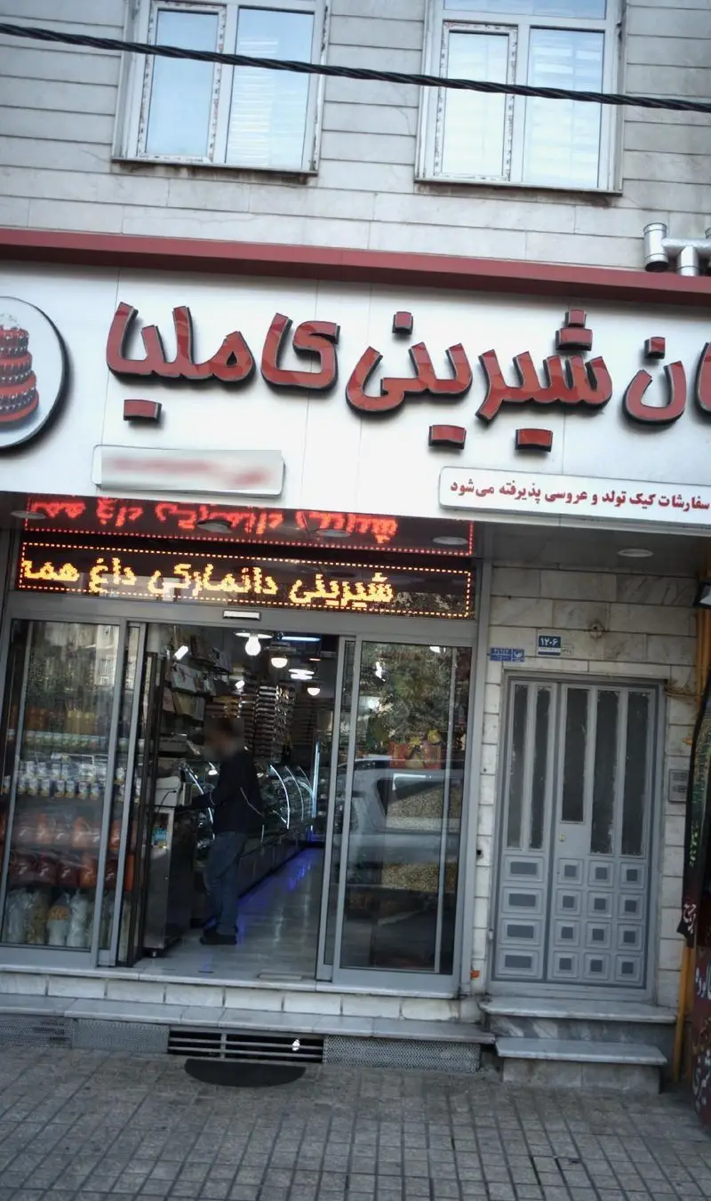 نمای جلوی قنادی کاملیا، فروشگاه شیرینی با تابلو روشن، شیرینی دانمارکی داغ و پذیرش سفارشات کیک تولد و عروسی.