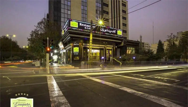 تصویری جذاب از نمای بیرونی کافه رستوران و کافی شاپ لوپتو در تهران، شب هنگام با نورپردازی زیبا و حرکت خودروها در خیابان.