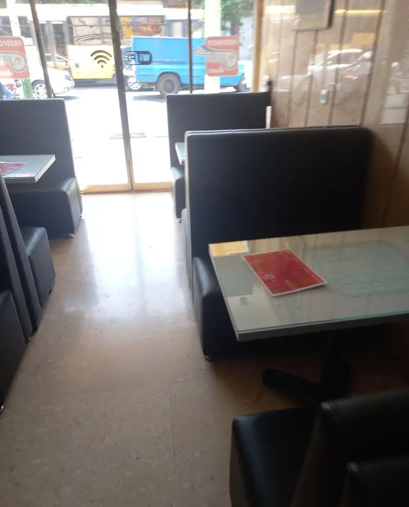 نمایی از فضای داخلی فست فود نمکدون، شامل سالن غذاخوری با میزهای شیشه‌ای و مبلمان راحت چرمی و پنجره مشرف به خیابان.