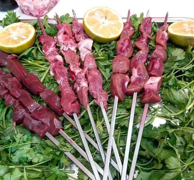 نمای نزدیک از سیخ‌های کباب جگر، دل و قلوه تازه و لذیذ، چیده شده روی سبزیجات معطر با برش‌های لیمو در جگرسرای پنج دری.