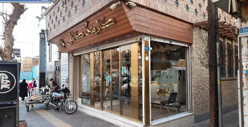 تصویر کسب و کار کترینگ کاظمی، نمای کامل ورودی با درهای شیشه‌ای و سردر چوبی با حروف طلایی. فضایی دلنشین و خدماتی برای مشتریان.