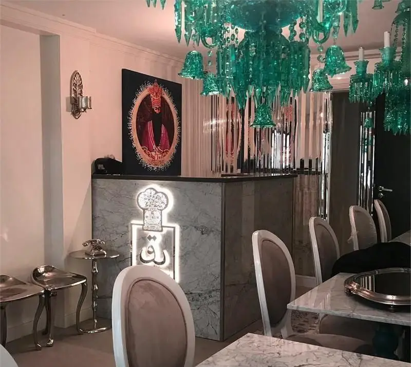 فضای داخلی لوکس و مدرن مطبخ قاجاری، با دکوراسیون الهام گرفته از دوره قاجار، شامل لوستر سبز و میزهای مرمرین.