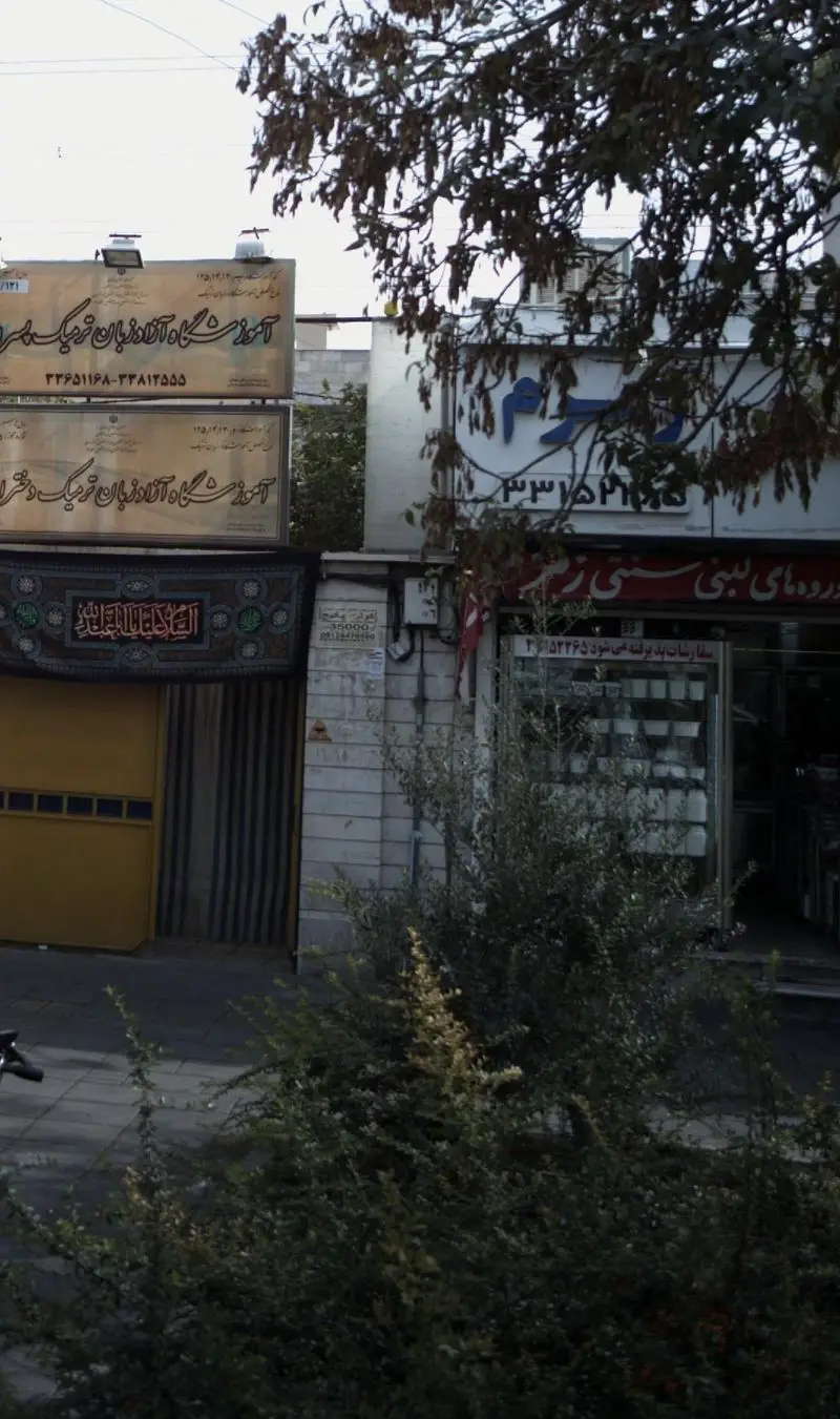 تصویری از نمای بیرونی فروشگاه لبنیات سنتی زمزم، شامل تابلوی مغازه و ویترین محصولات لبنی. در کنار آموزشگاه و خیابان شلوغ شهری با درختان.