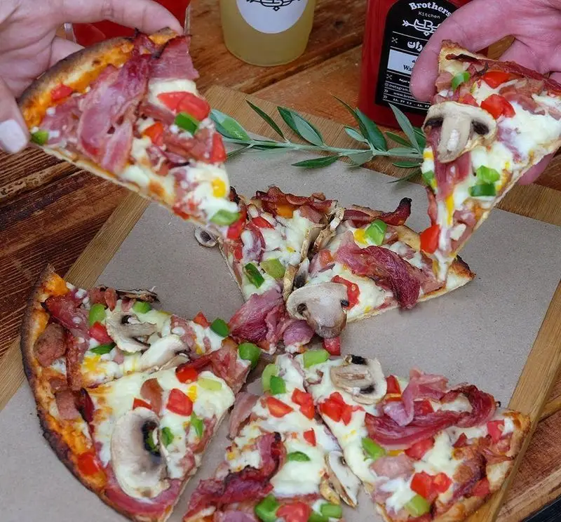 پیتزا مخصوص گوشت و سبزیجات چلوکبابی برادران: تکه‌های پیتزای لذیذ با بیکن، قارچ، فلفل و پنیر روی تخته چوبی، آماده سرو.