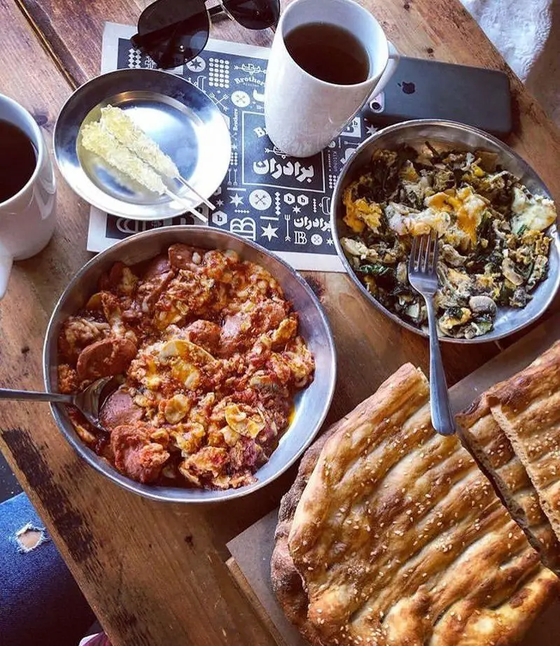 میز صبحانه کامل در رستوران چلوکبابی برادران شامل املت سبزیجات، سوسیس تخم‌مرغ، نان داغ، چای و نبات. لذت طعم ایرانی.