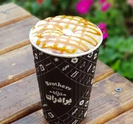 نوشیدنی کاراملی دلچسب از چلوکبابی برادران، سرو شده در فنجانی با نام "برادرز کیچن" بر روی میز چوبی.