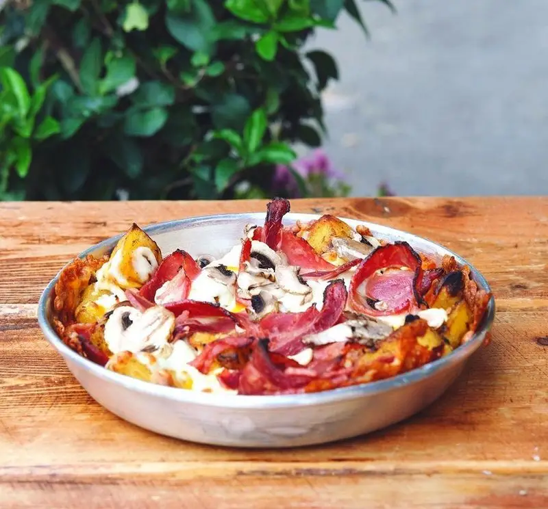 کاسرول سیب‌زمینی لذیذ و خانگی چلوکبابی برادران با قارچ، ژامبون و پنیر، سرو شده روی میز چوبی در فضای دلنشین باز.