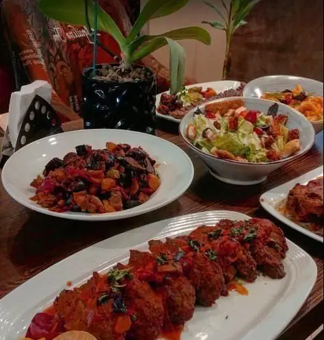 تصویری جذاب از میز مملو از غذاهای کافی شاپ شکوفه: کوفته سس‌دار، سالاد سبز و خوراک سبزیجات، آماده برای سرو.