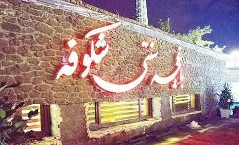 تصویری از نمای شب کافی شاپ شکوفه با تابلوی نئونی درخشان روی دیوار سنگی و پنجره‌های روشن، محیطی دلپذیر برای تجربه قهوه