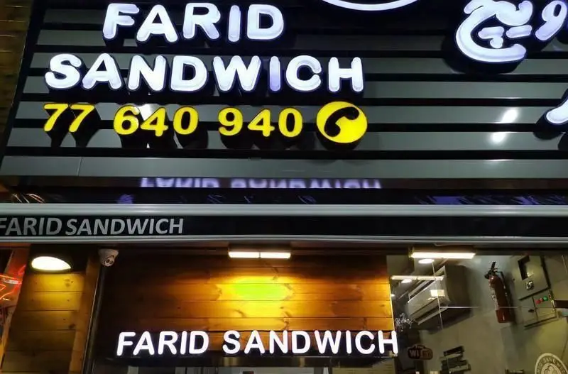 نمای بیرونی تابلوی روشن ساندویچی فرید با لوگو و شماره تماس 77 640 940 برای سفارش انواع ساندویچ‌های خوشمزه.