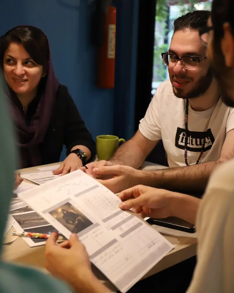 دورهمی پرشور در کافه برد، مشتریان در حال همفکری و بررسی جزئیات یک طرح یا بازی جدید، محیطی ایده‌آل برای خلاقیت و لذت.